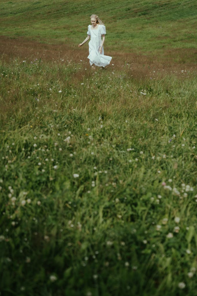 A serene scene of a woman in a white dress walking through a verdant meadow.