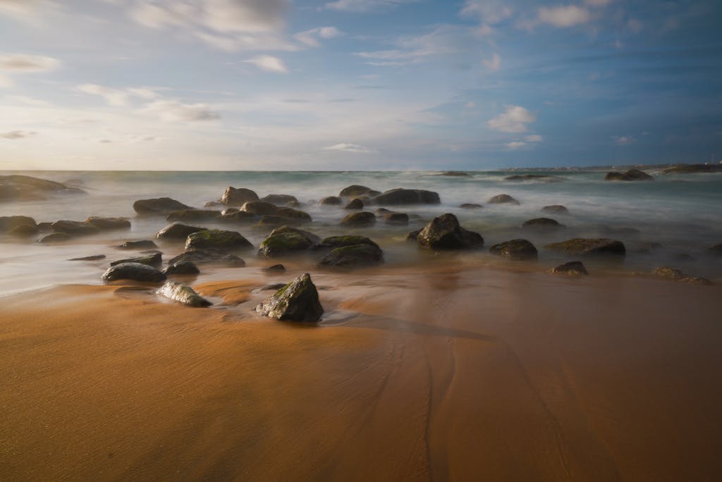 Peaceful sandy beach with ocean waves and rocks at sunset creating a tranquil atmosphere.
