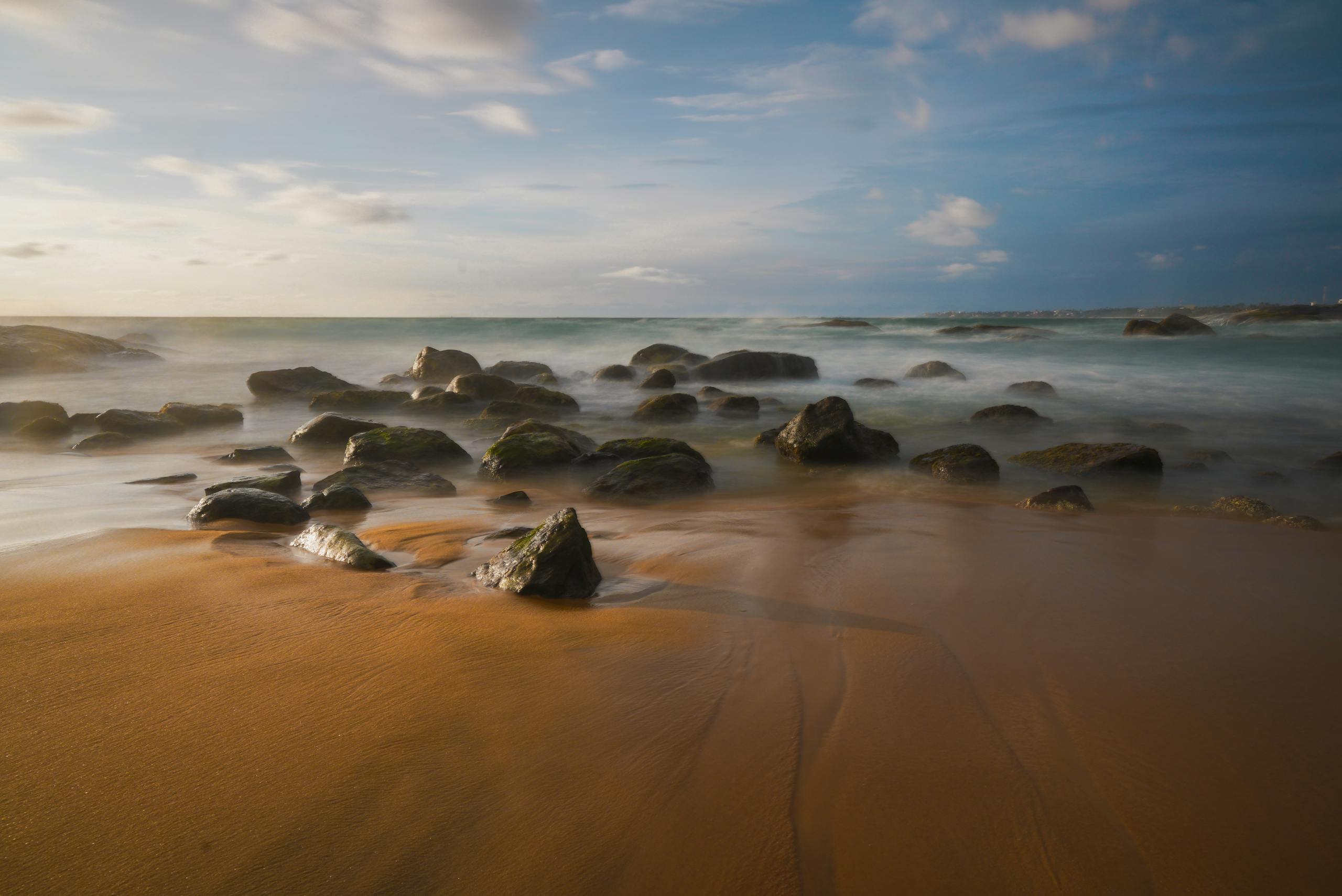 Peaceful sandy beach with ocean waves and rocks at sunset creating a tranquil atmosphere.